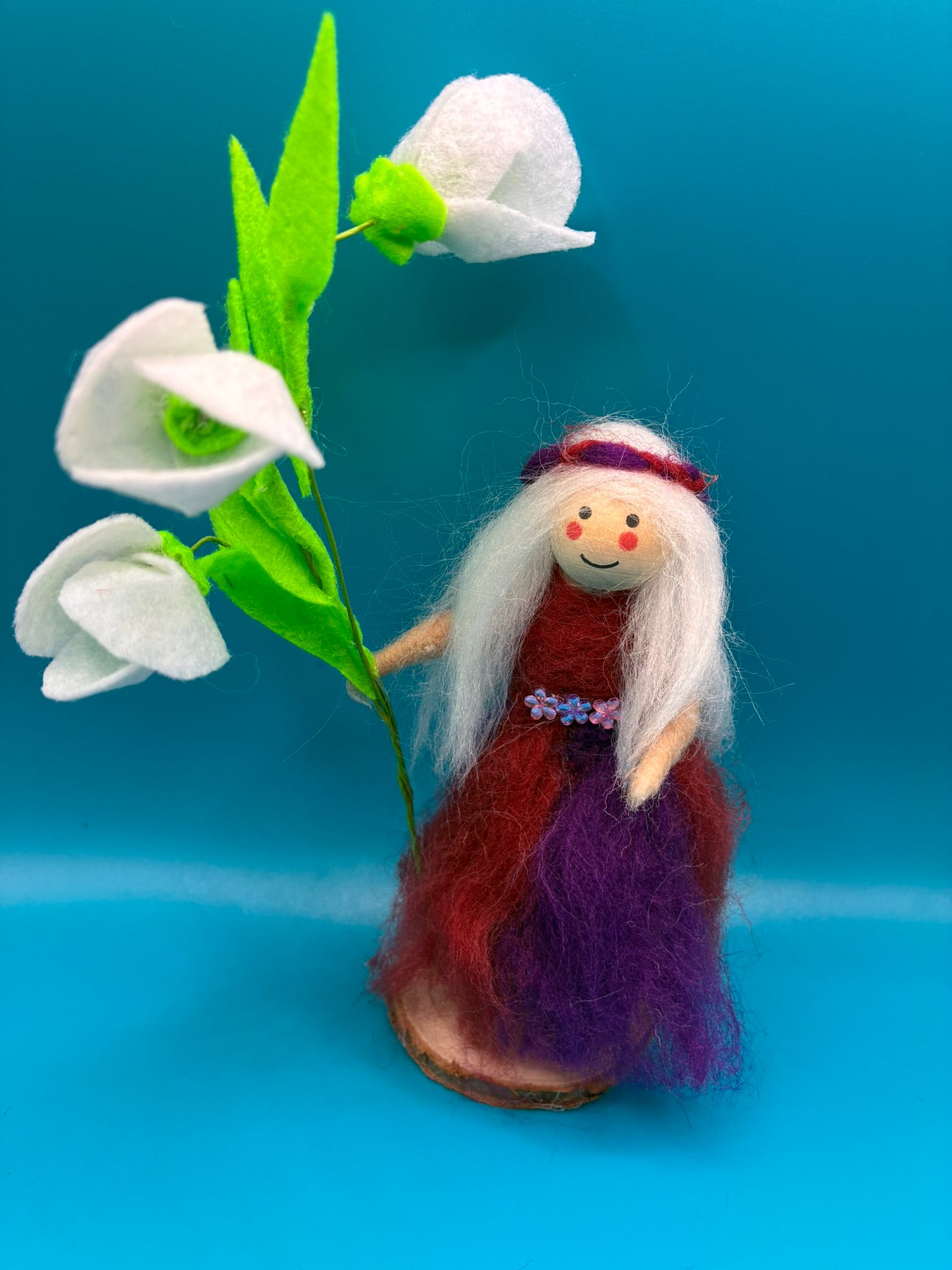 Needle felt fairy with white hair holding white flowers on wood slice