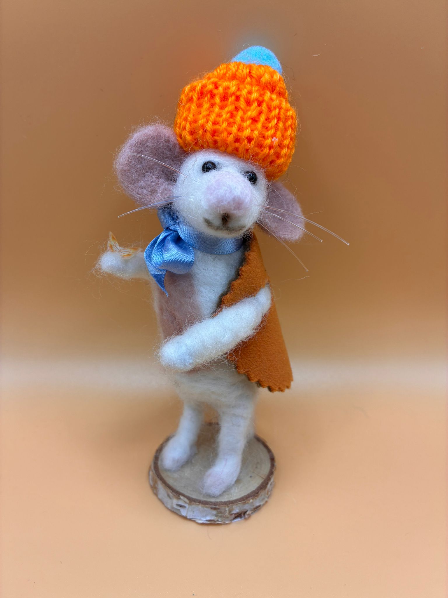 Needle felt mouse in orange knitted hat and cape on wood slice