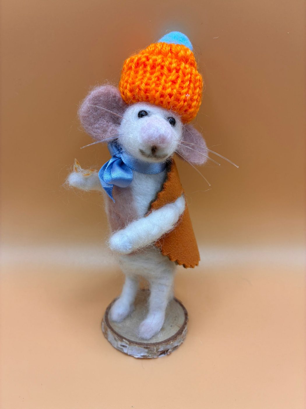 Needle felt mouse in orange knitted hat and cape on wood slice